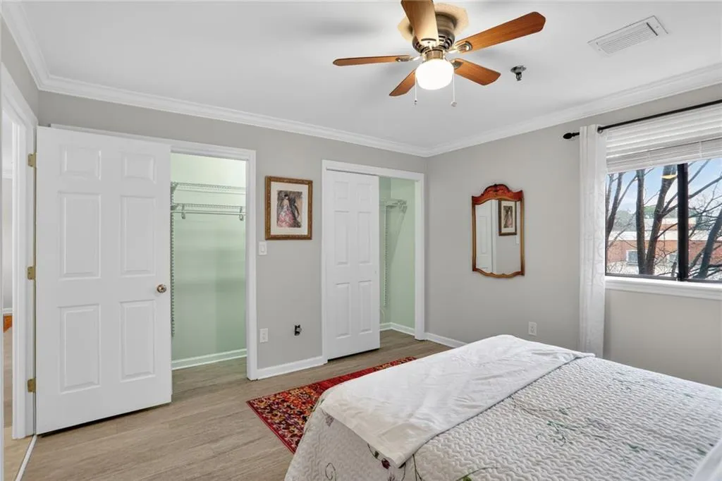 Bedroom with a spacious closet, ornamental molding, light wood-style flooring, and a ceiling fan
