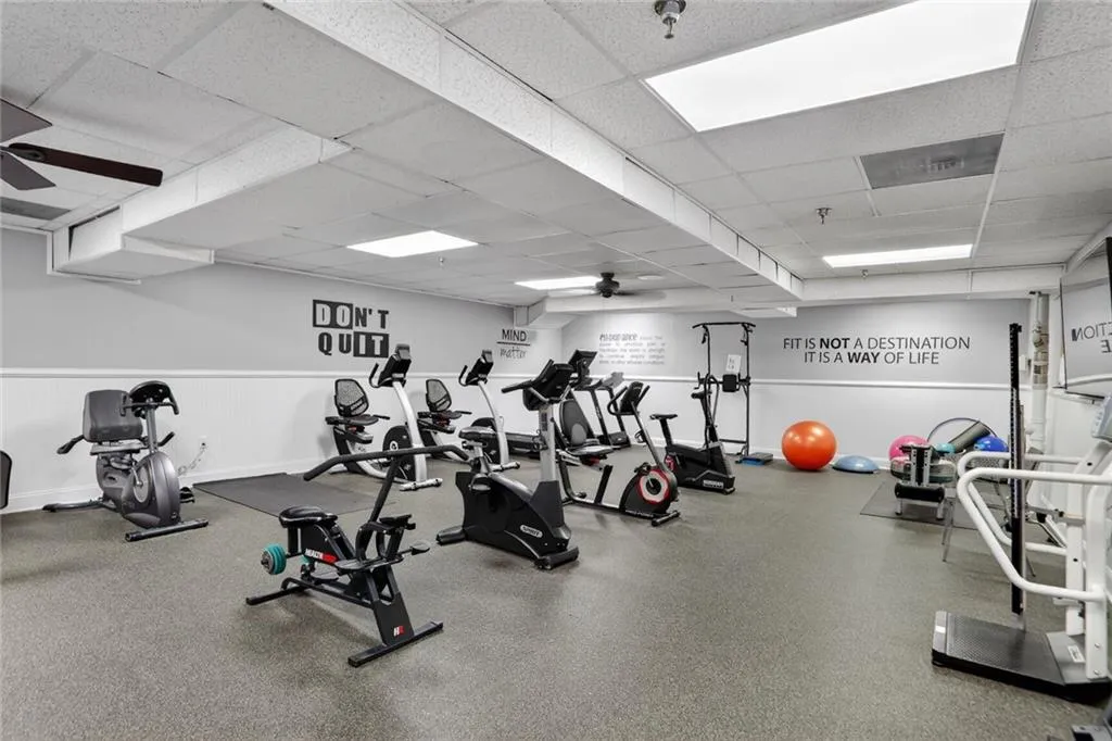 Exercise room featuring a ceiling fan, a drop ceiling, and wainscoting