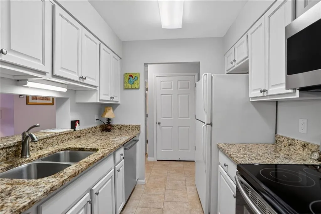 Kitchen with white cabinetry, stainless steel appliances, light stone counters, and light tile patterned floors