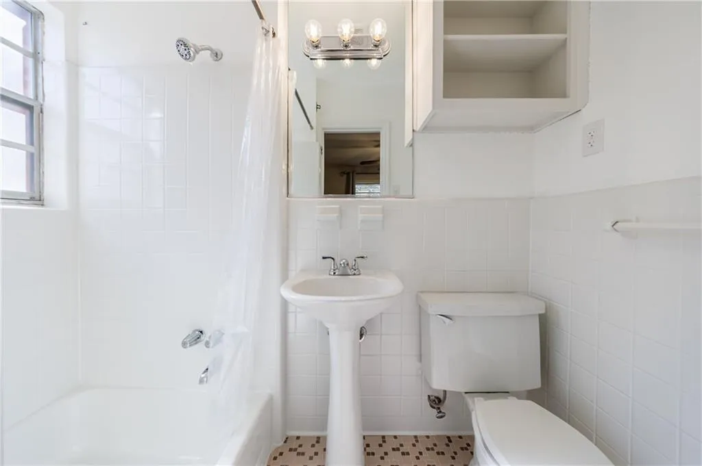 Full bathroom featuring shower / bath combo with shower curtain, tile walls, and wainscoting Full bathroom featuring shower / bath combo with shower curtain, tile walls, and wainscoting