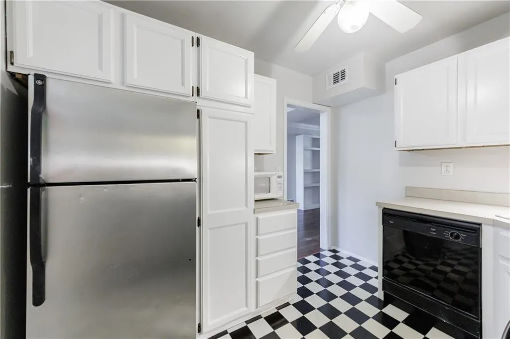 Kitchen featuring freestanding refrigerator, black dishwasher, light countertops, white cabinets, and light floors Kitchen featuring freestanding refrigerator, black dishwasher, light countertops, white cabinets, and light floors