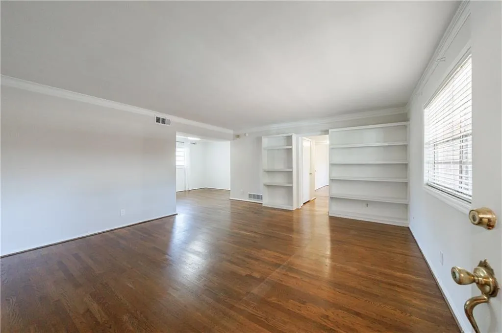 Empty room with dark wood-style flooring, ornamental molding, and built in shelves Empty room with dark wood-style flooring, ornamental molding, and built in shelves