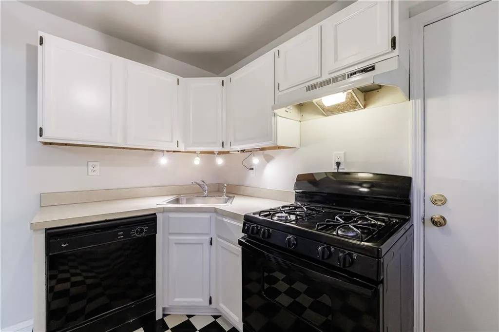 Kitchen featuring black appliances, under cabinet range hood, white cabinets, and light countertops Kitchen featuring black appliances, under cabinet range hood, white cabinets, and light countertops