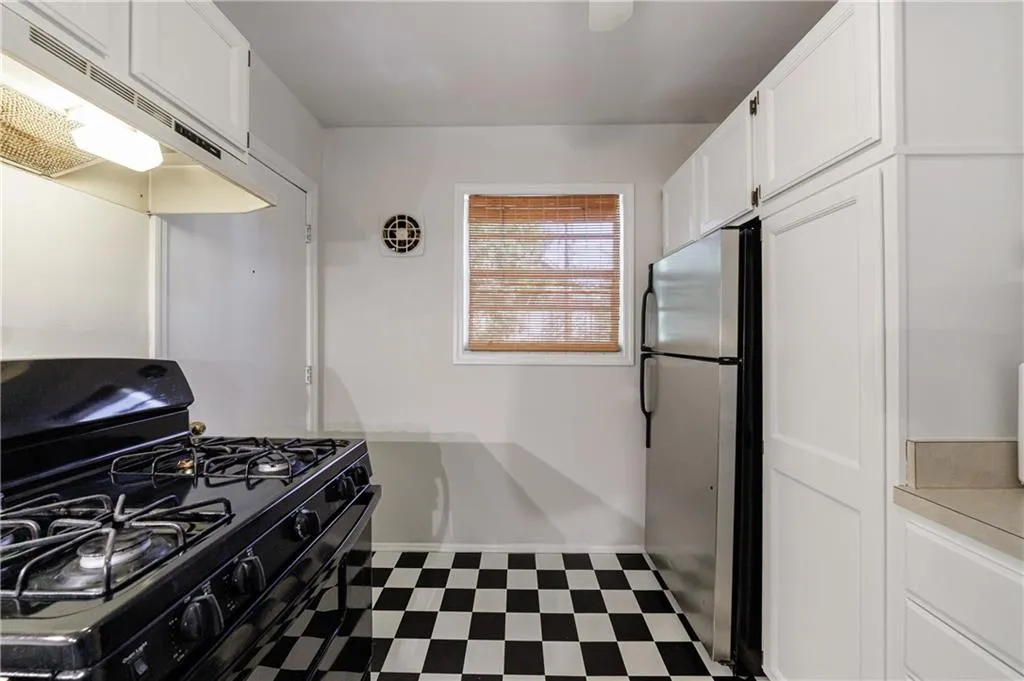 Kitchen with black gas range, under cabinet range hood, light floors, white cabinets, and freestanding refrigerator Kitchen with black gas range, under cabinet range hood, light floors, white cabinets, and freestanding refrigerator