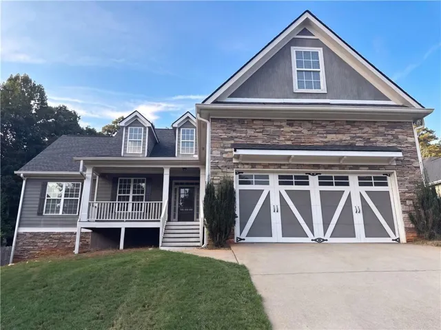 Two-story residence featuring a covered front porch, dormer windows, stone veneer accents, and a two-car garage with decorative hardware