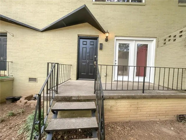 Exterior entry featuring a painted brick facade, concrete steps with wrought iron railings, a black paneled entry door, and a traditional outdoor wall lantern