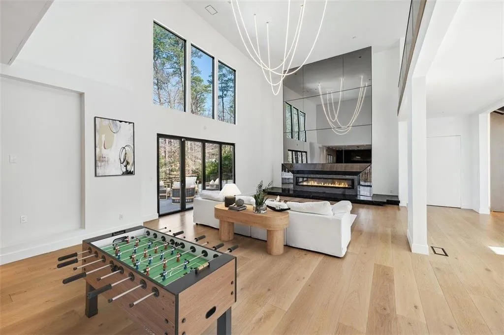 Rec room with a glass covered fireplace, light wood-style flooring, a chandelier, and a towering ceiling