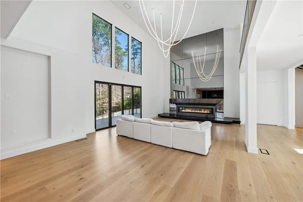 Living room featuring a chandelier, light wood-style flooring, a glass covered fireplace, and a towering ceiling