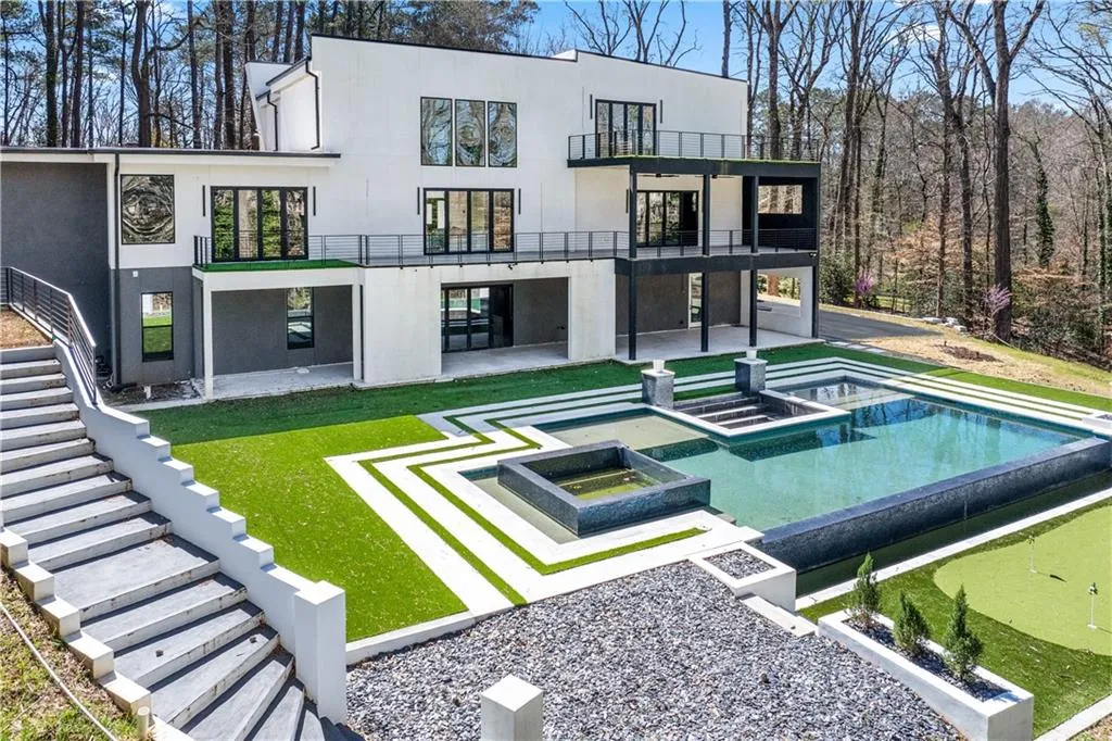 Back of house featuring a patio area, a putting green, stairs, a balcony, and stucco siding