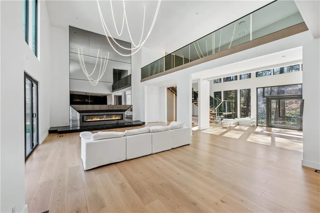 Unfurnished living room featuring stairs, a high ceiling, light wood-style flooring, and a glass covered fireplace