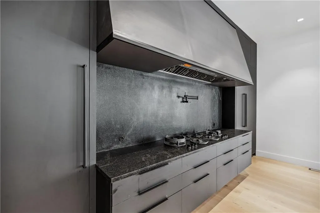 Kitchen featuring exhaust hood, modern cabinets, dark stone countertops, and light wood finished floors