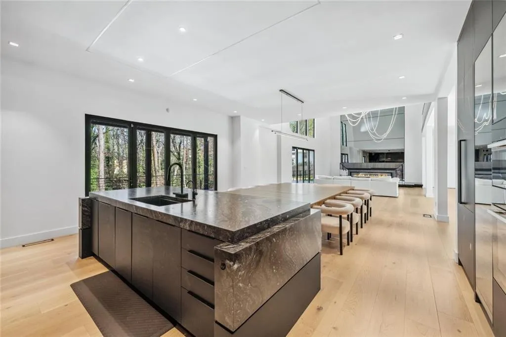 Kitchen with modern cabinets, an island with sink, dark stone countertops, dark brown cabinets, and light wood-style flooring