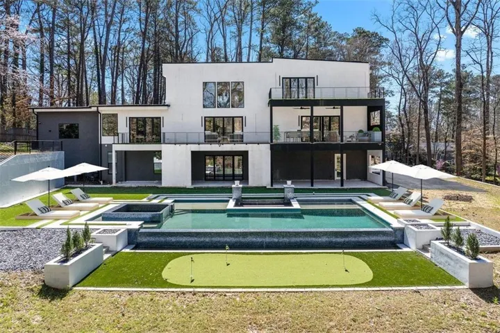 Rear view of property featuring a hot tub, a putting green, a patio area, and a balcony