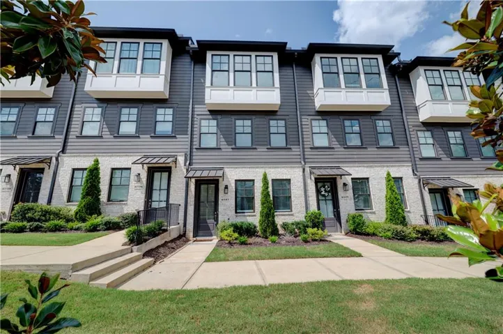 Modern townhome exterior featuring a grey siding upper level, light-toned brick lower level, and black-framed windows