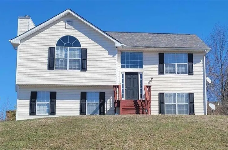 Split-level residence featuring light-toned siding, a prominent front entry with a dark door, and multiple windows with dark shutters