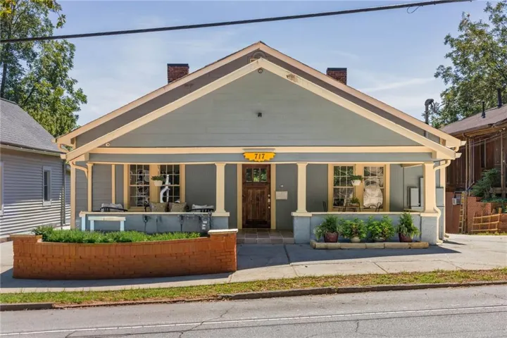 Gabled roofline with light blue siding, full-width covered porch, brick planter box, and a wood-finish entry door