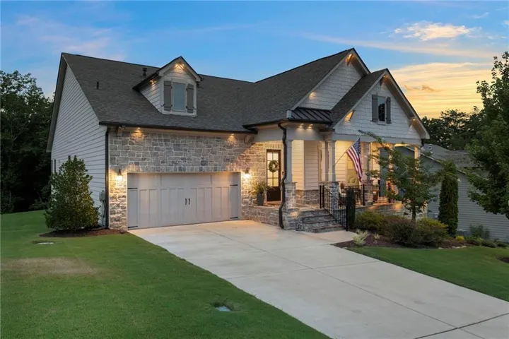 Stone and siding exterior with a covered front porch, attached two-car garage, and a concrete driveway
