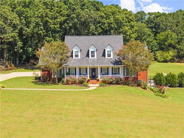 Brick residence featuring a covered front porch with white railing, three dormer windows, and a paved driveway
