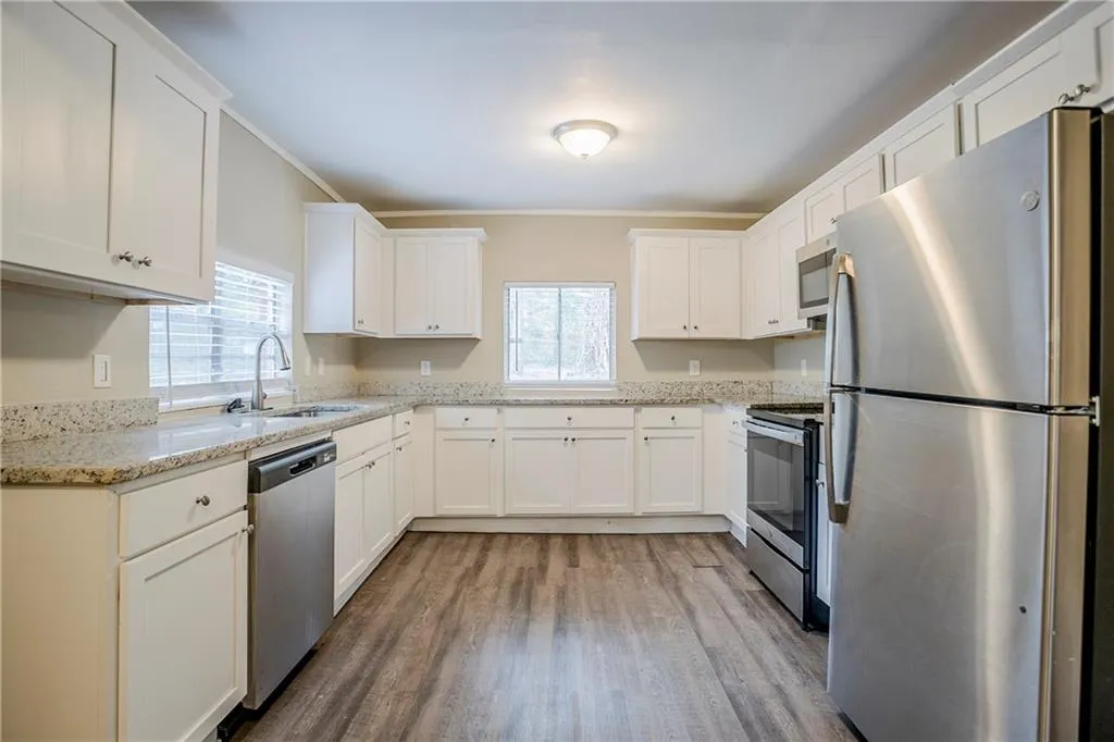 Kitchen featuring light stone counters, sink, white cabinetry, and stainless steel appliances