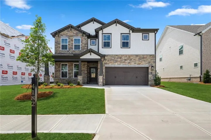 Contemporary two-story residence featuring stone and horizontal siding accents, a prominent front entry, a two-car garage, a concrete driveway, and a manicured front lawn with a young tree