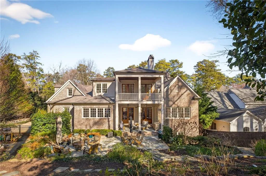Back of house featuring a patio area, a chimney, brick siding, a balcony, and french doors