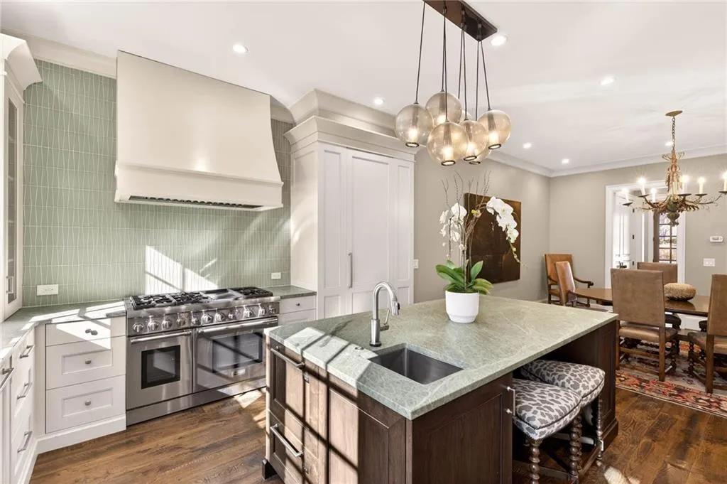 Kitchen with double oven range, custom range hood, light stone counters, a chandelier, and decorative light fixtures