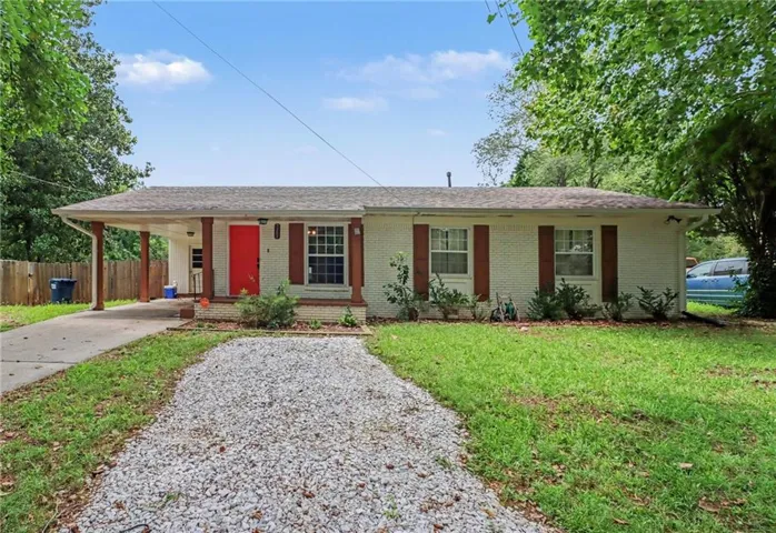 Single-story home featuring a white brick exterior and a vibrant red entry door