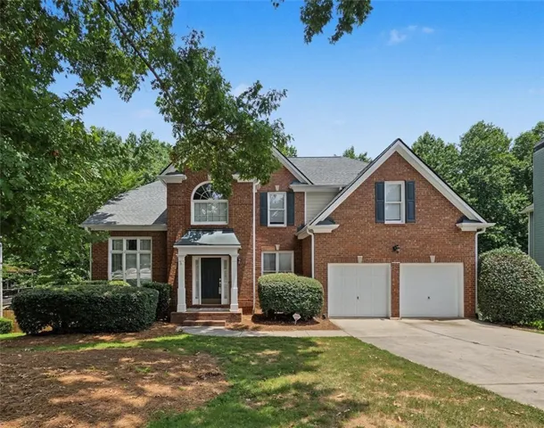 Brick facade residence featuring a two-car garage, a covered entry with columns, gabled rooflines, and mature landscaping