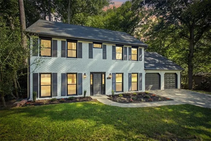Two-story brick exterior with dark shutters, dual garage doors, a paved driveway, and mature trees