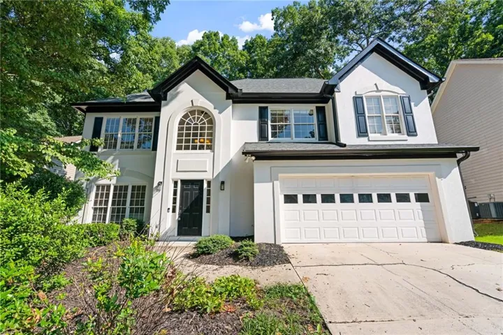 Stucco facade residence featuring a two-car garage with panel windows, a prominent arched window, multiple large windows with black shutters, and dark trim details
