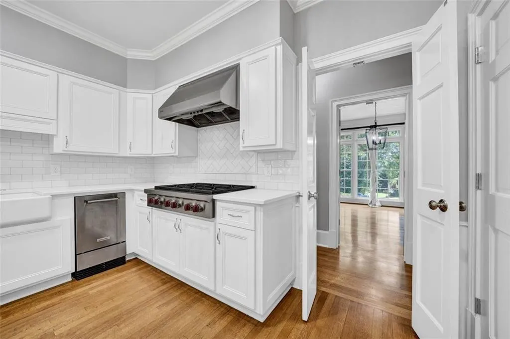 Kitchen featuring wall chimney range hood, tasteful backsplash, white cabinets, and light wood-type flooring