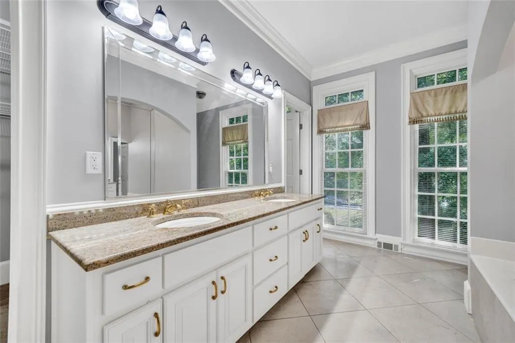 Bathroom featuring ornamental molding, a bath to relax in, tile floors, large vanity, and dual sinks