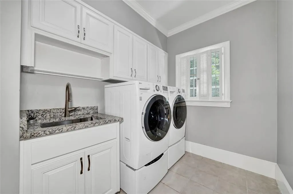 Washroom featuring cabinets, light tile flooring, washing machine and clothes dryer, ornamental molding, and sink
