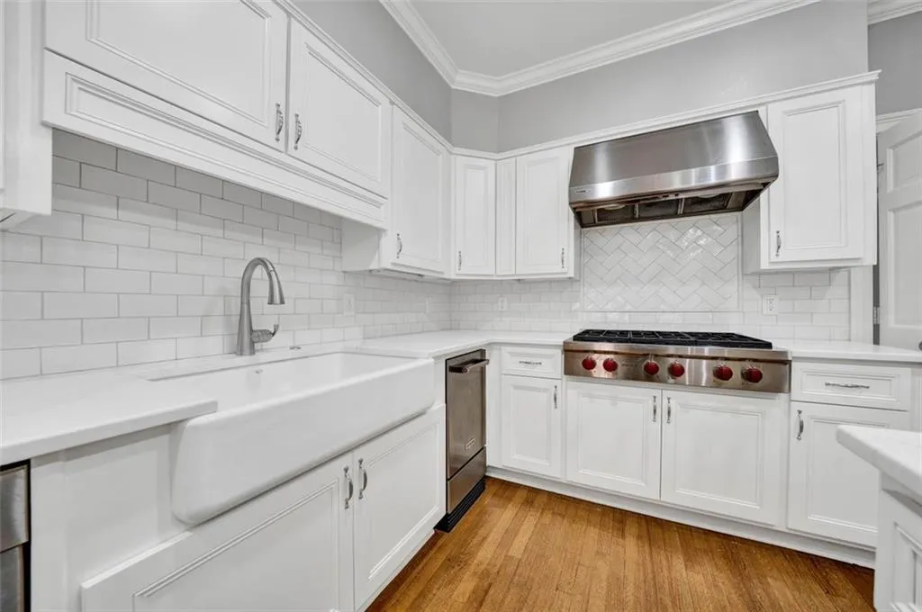 Kitchen featuring wall chimney exhaust hood, light hardwood / wood-style flooring, backsplash, and white cabinetry