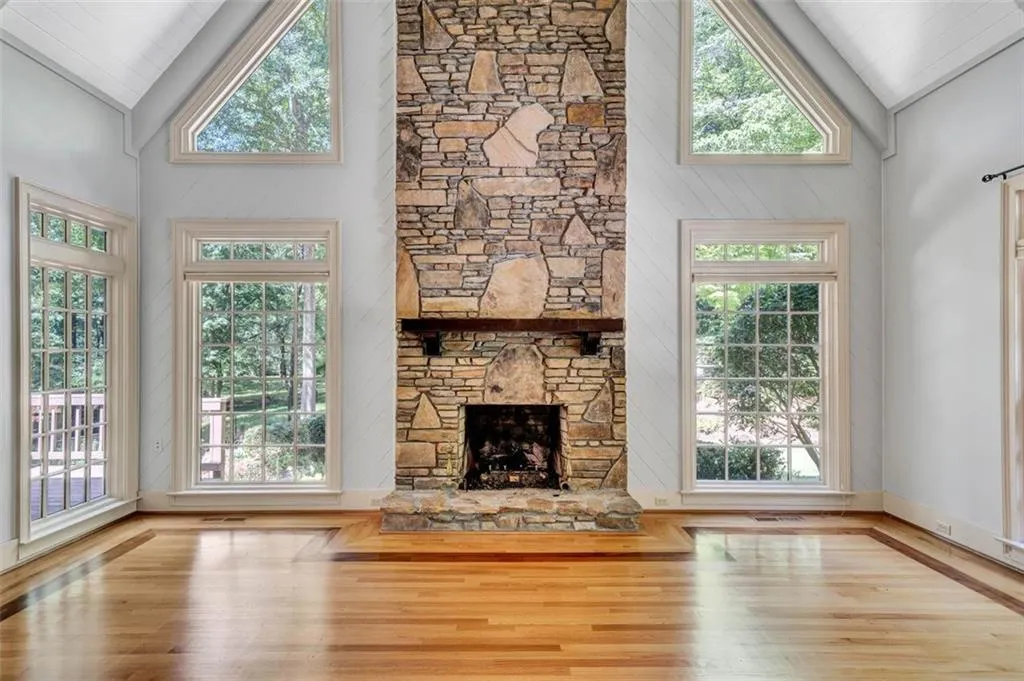Unfurnished living room featuring a stone fireplace, high vaulted ceiling, and wood-type flooring