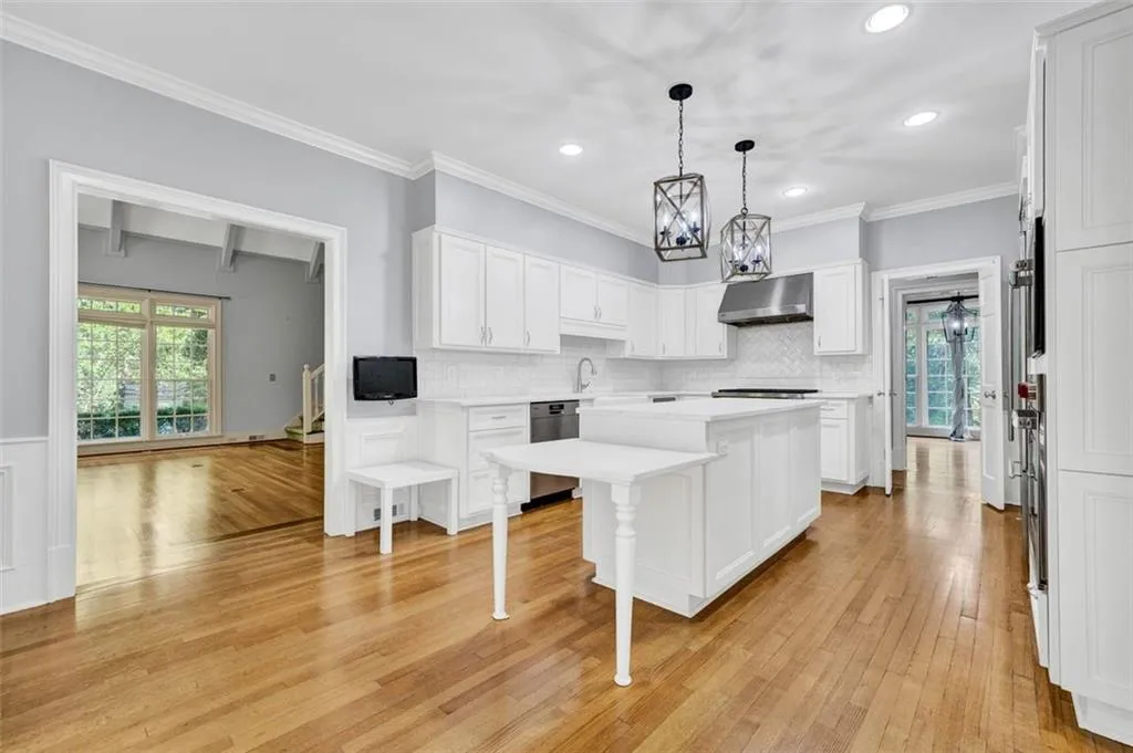 Kitchen featuring wall chimney range hood, hanging light fixtures, tasteful backsplash, stainless steel dishwasher, and light wood-type flooring