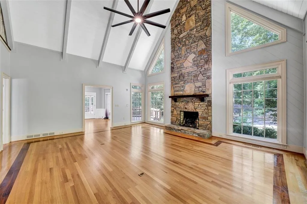 Unfurnished living room featuring a stone fireplace, high vaulted ceiling, light hardwood / wood-style floors, and plenty of natural light