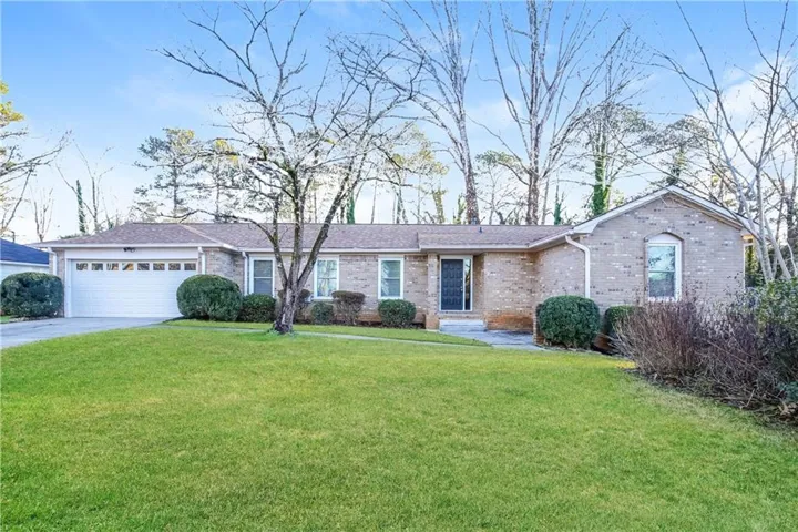 Brick exterior featuring a two-car garage, front lawn, and mature landscaping