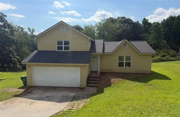 Two-story residence featuring light yellow siding, a dark gray shingle roof, a two-car garage, and an inviting front entry