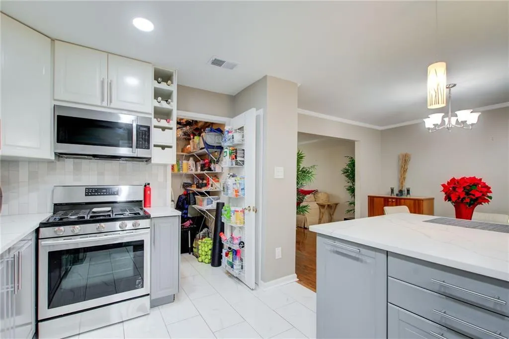 Kitchen with appliances with stainless steel finishes, decorative backsplash, hanging light fixtures, open shelves, and light stone countertops