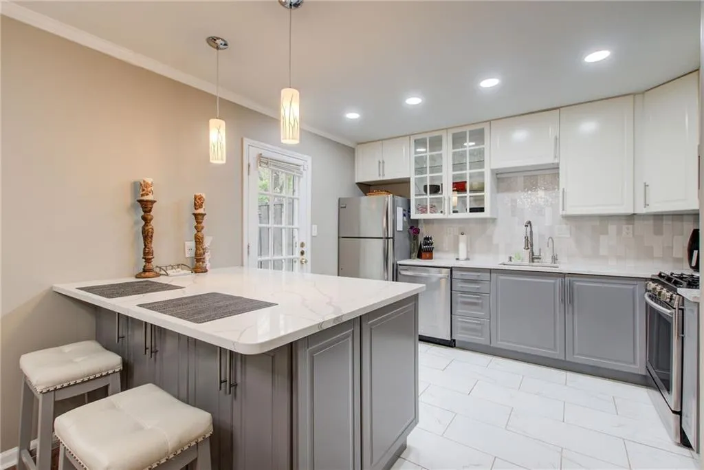 Kitchen featuring a breakfast bar, gray cabinetry, glass insert cabinets, white cabinetry, and appliances with stainless steel finishes