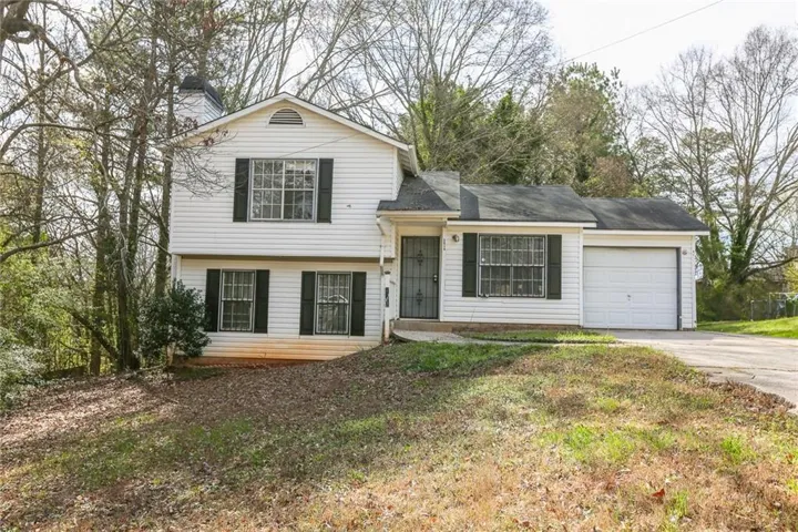 Tri-level home with concrete driveway, a garage, a front lawn, and a chimney