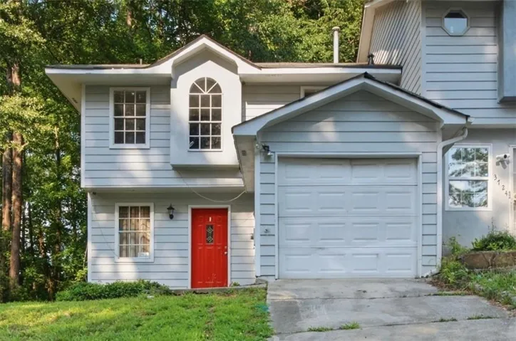 Light blue siding exterior featuring a prominent red front door, white-framed windows, an arched multi-pane window, and an attached garage with a white panel door