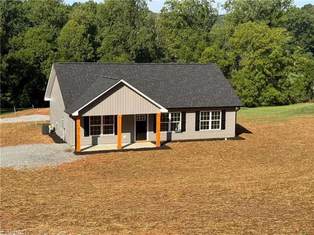 Siding exterior with black shutters, dark shingle roof, and a gravel driveway