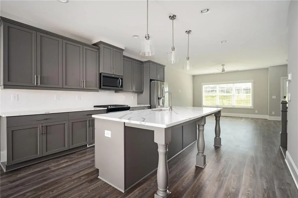 Kitchen with pendant lighting, appliances with stainless steel finishes, an island with sink, gray cabinets, and light stone counters