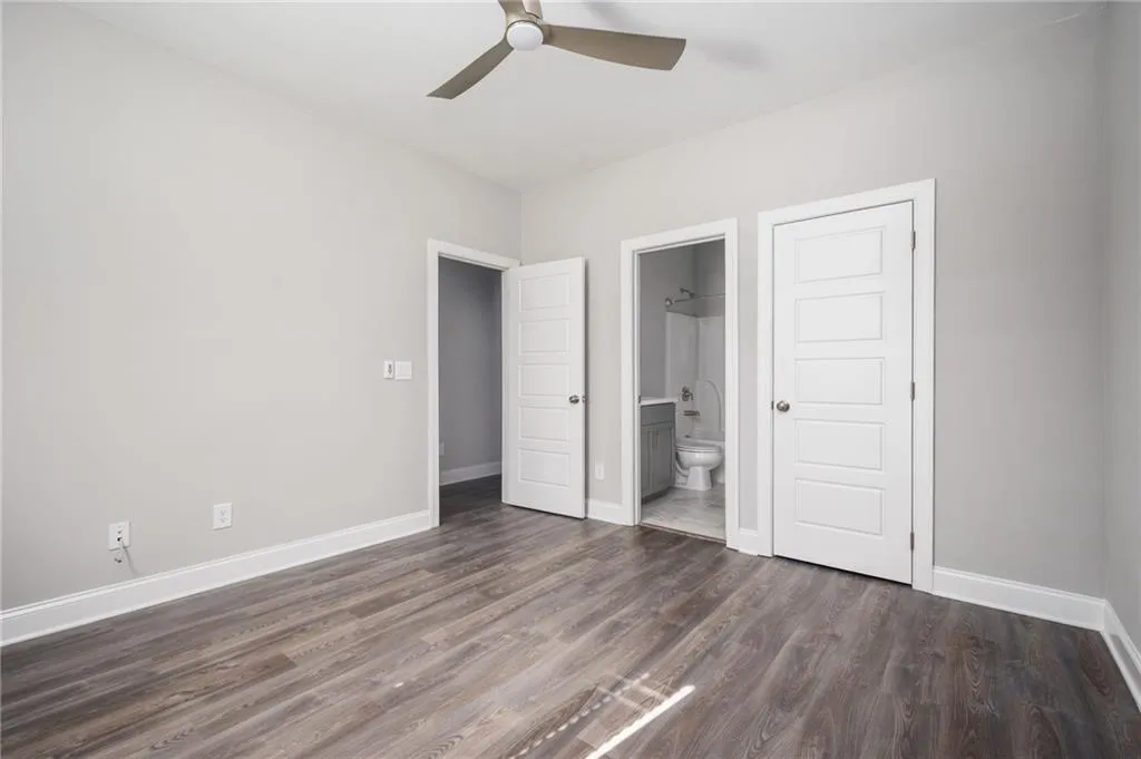 Unfurnished bedroom with a ceiling fan, dark wood-style floors, ensuite bath, and a closet