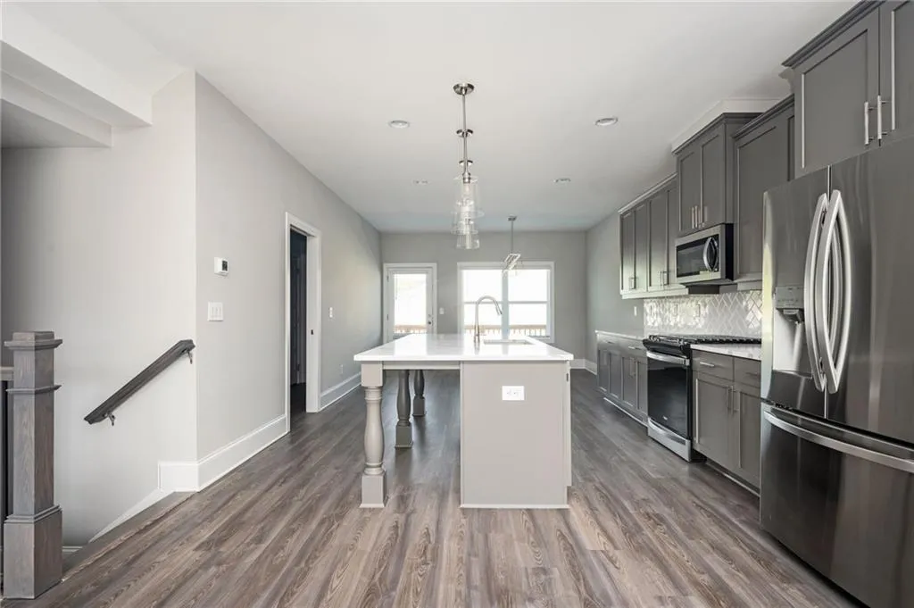Kitchen featuring stainless steel appliances, gray cabinets, pendant lighting, an island with sink, and a breakfast bar area