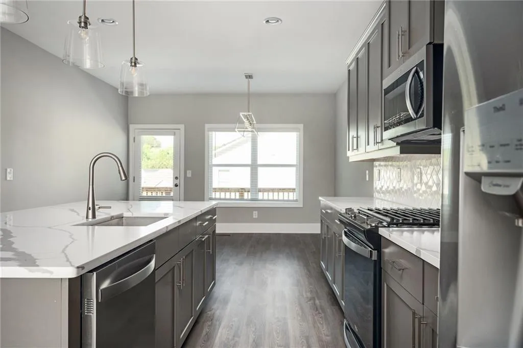 Kitchen with appliances with stainless steel finishes, pendant lighting, dark wood finished floors, light stone counters, and recessed lighting