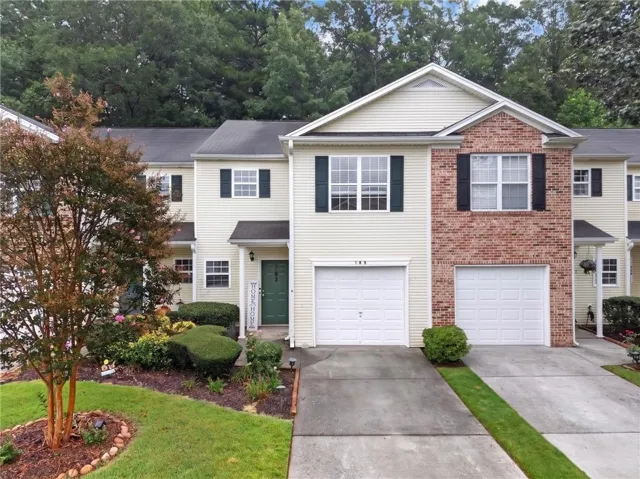 Exterior featuring siding and brick accents, attached garage, paved driveway, and landscaped front yard