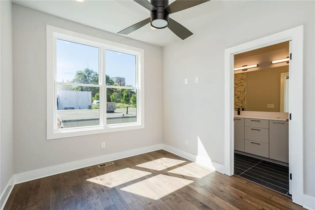Unfurnished bedroom with ensuite bathroom, multiple windows, dark hardwood / wood-style floors, and ceiling fan